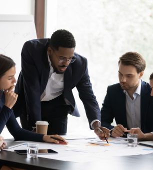 Confident african American male boss work cooperate with diverse team at office briefing, focused biracial businessman head meeting, collaborate discuss business ideas with colleagues at meeting