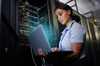 Laptop, network and data center with a black woman it support engineer working in a dark server room. Computer, cybersecurity and analytics with a female programmer problem solving or troubleshooting.